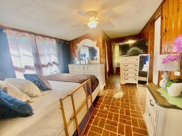 bedroom featuring a textured ceiling, wood walls, ceiling fan, and brick floor
