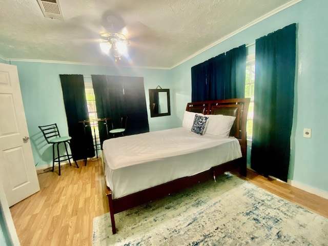 bedroom with crown molding, wood finished floors, visible vents, and multiple windows
