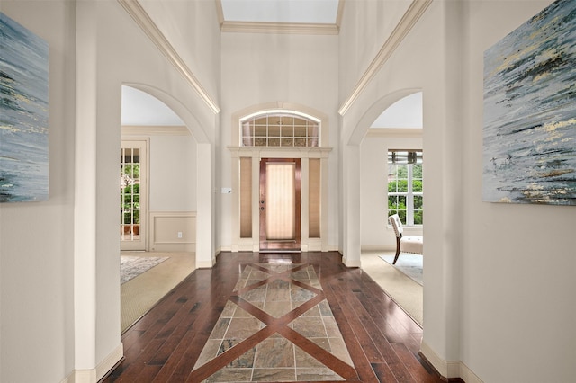entryway with crown molding, arched walkways, wood finished floors, and a towering ceiling