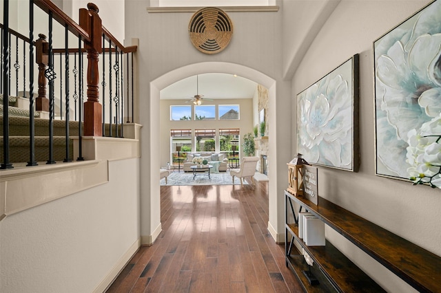 corridor featuring baseboards, a high ceiling, stairway, arched walkways, and dark wood finished floors