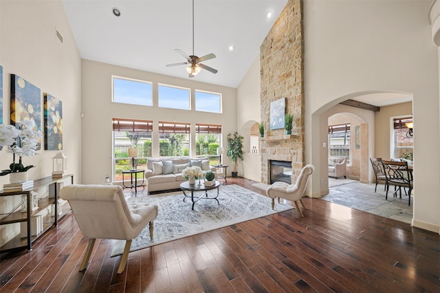 living room with hardwood / wood-style floors, a fireplace, ceiling fan, high vaulted ceiling, and arched walkways