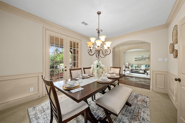 dining area with light colored carpet, wainscoting, a decorative wall, arched walkways, and visible vents