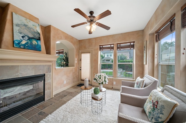 living room with a tiled fireplace, baseboards, ceiling fan, and stone tile floors