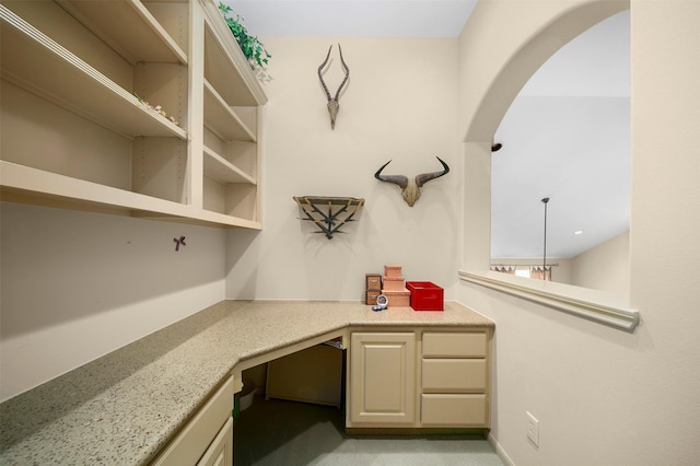 unfurnished office featuring arched walkways, built in desk, and light colored carpet