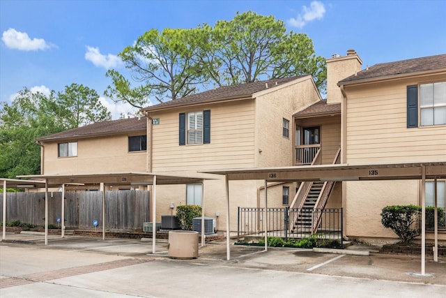 rear view of property featuring covered parking, central air condition unit, stairway, and fence