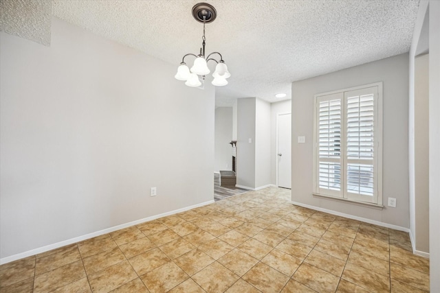spare room featuring a textured ceiling, a chandelier, and baseboards
