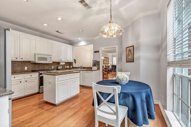 kitchen with an inviting chandelier, ornamental molding, white appliances, and white cabinetry