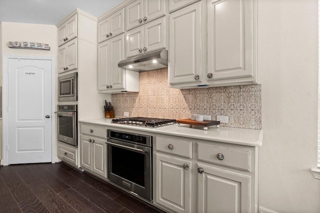 kitchen with under cabinet range hood, stainless steel appliances, backsplash, and light countertops