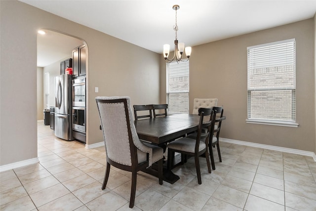 dining room featuring baseboards, arched walkways, light tile patterned flooring, and a chandelier