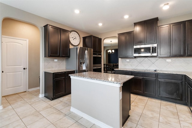 kitchen featuring light stone countertops, a center island, tasteful backsplash, arched walkways, and appliances with stainless steel finishes