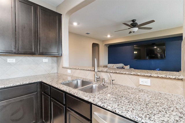 kitchen featuring light stone countertops, a sink, arched walkways, a ceiling fan, and backsplash