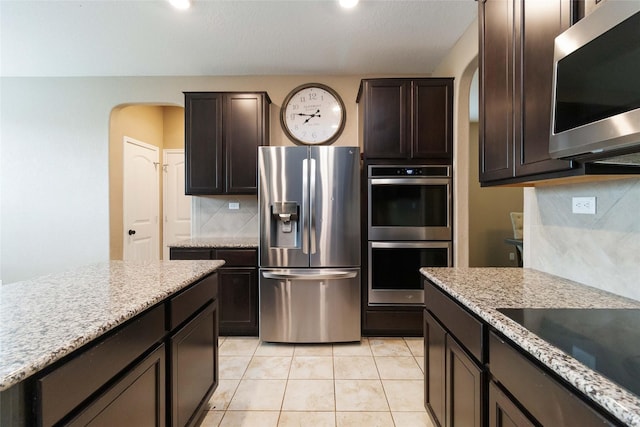 kitchen with backsplash, dark brown cabinetry, light stone countertops, and stainless steel appliances