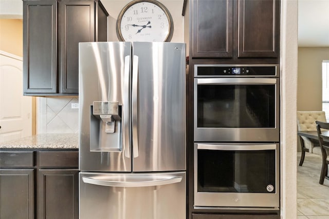 kitchen featuring dark brown cabinets, light stone countertops, appliances with stainless steel finishes, and decorative backsplash