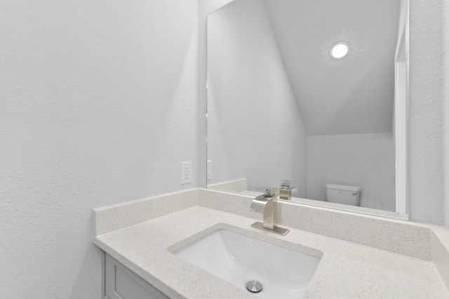half bath with vanity, a textured wall, and toilet