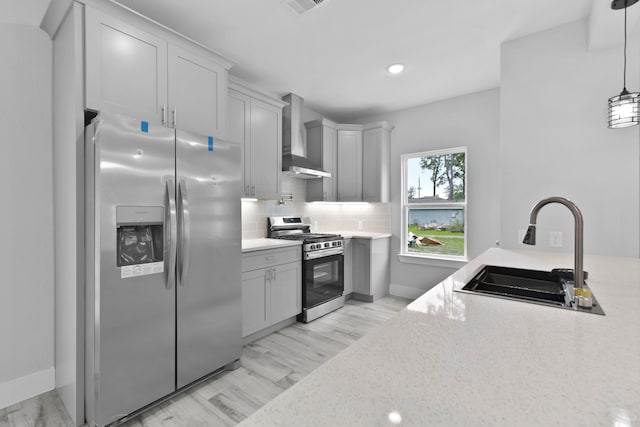 kitchen with decorative backsplash, wall chimney range hood, a sink, hanging light fixtures, and stainless steel appliances