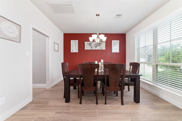 dining area with visible vents, an accent wall, a notable chandelier, and a healthy amount of sunlight