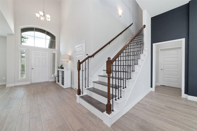 foyer featuring a high ceiling, light wood-type flooring, stairs, and a notable chandelier