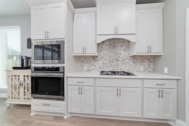kitchen with appliances with stainless steel finishes, tasteful backsplash, light countertops, white cabinets, and light wood-style floors
