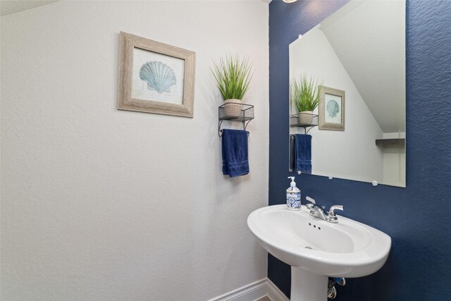 bathroom featuring baseboards, a sink, and vaulted ceiling