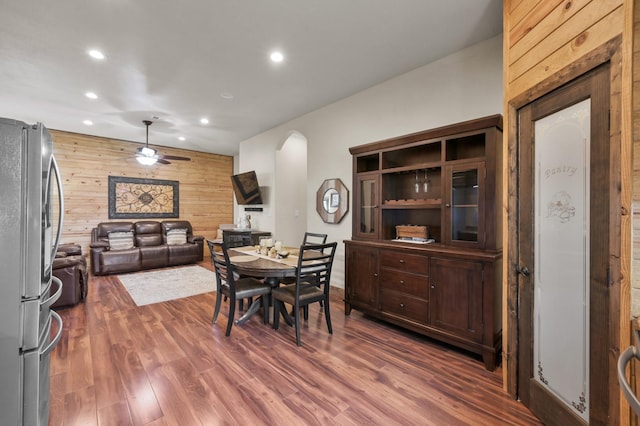 dining room with wooden walls, ceiling fan, arched walkways, recessed lighting, and wood finished floors