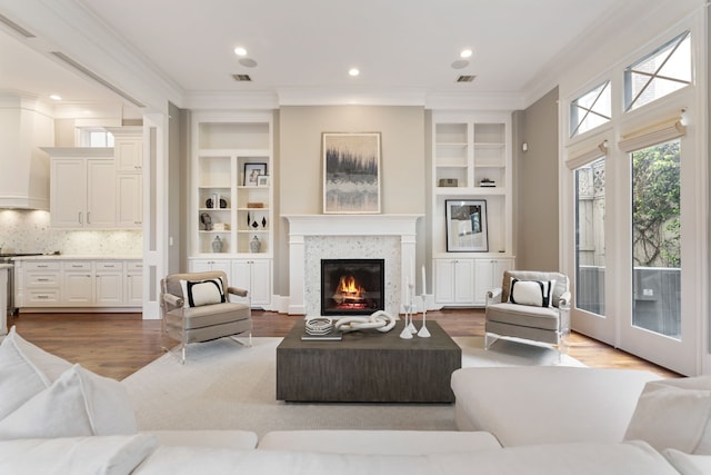 living room featuring ornamental molding, built in features, a glass covered fireplace, and wood finished floors