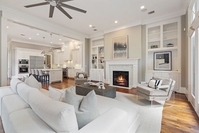 living area featuring a ceiling fan, visible vents, crown molding, light wood-type flooring, and a glass covered fireplace
