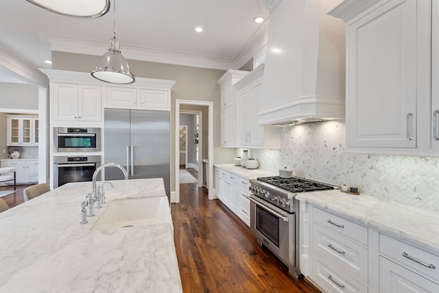 kitchen with white cabinets, high end appliances, a sink, and wall chimney exhaust hood