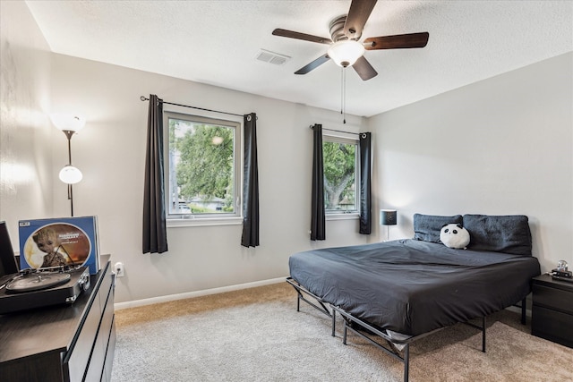 bedroom featuring baseboards, light carpet, a textured ceiling, and visible vents
