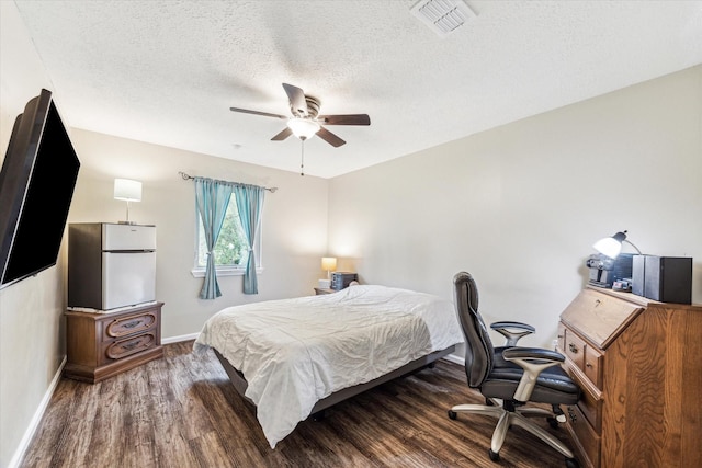 bedroom featuring a textured ceiling, freestanding refrigerator, baseboards, wood finished floors, and visible vents