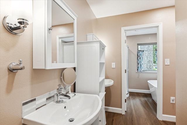 full bath featuring baseboards, a sink, a freestanding bath, and wood finished floors