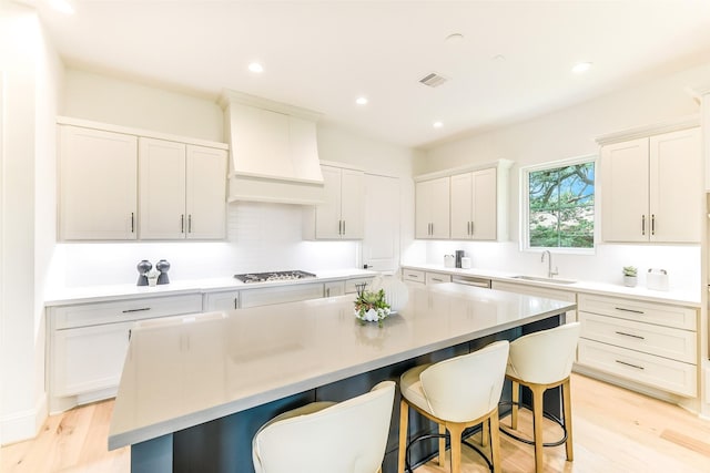 kitchen featuring a breakfast bar area, visible vents, a center island, a sink, and custom exhaust hood