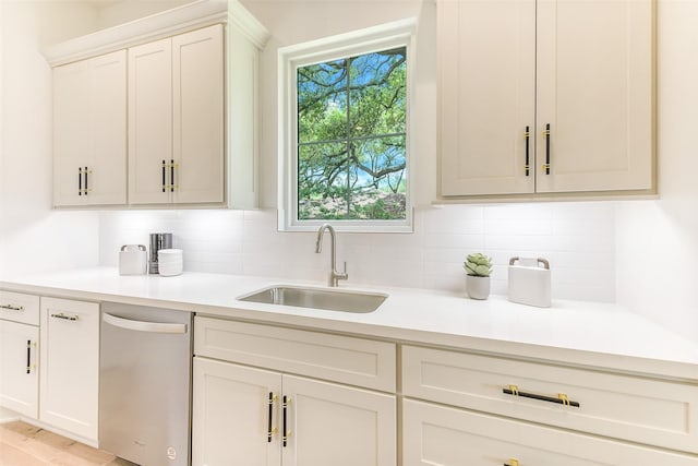 kitchen with stainless steel dishwasher, light countertops, white cabinetry, a sink, and backsplash