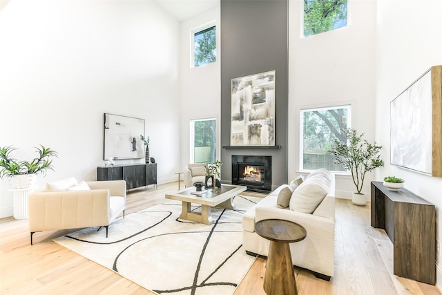 living area with baseboards, light wood finished floors, a towering ceiling, and a glass covered fireplace