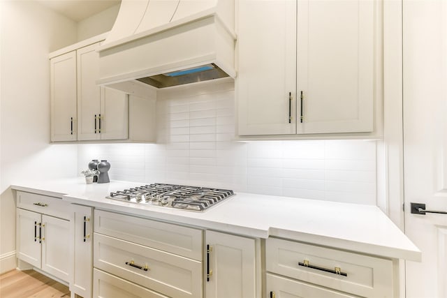kitchen featuring stainless steel gas stovetop, light countertops, decorative backsplash, and custom exhaust hood