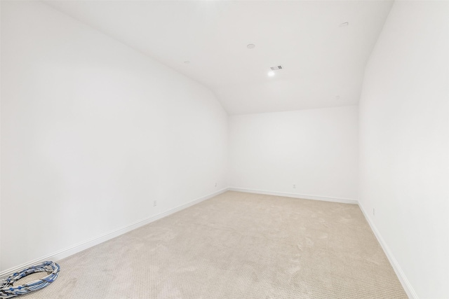spare room featuring baseboards, vaulted ceiling, light carpet, and visible vents