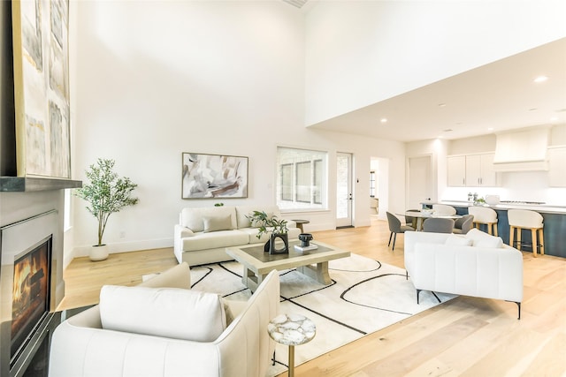 living room featuring a towering ceiling, baseboards, light wood finished floors, and a fireplace
