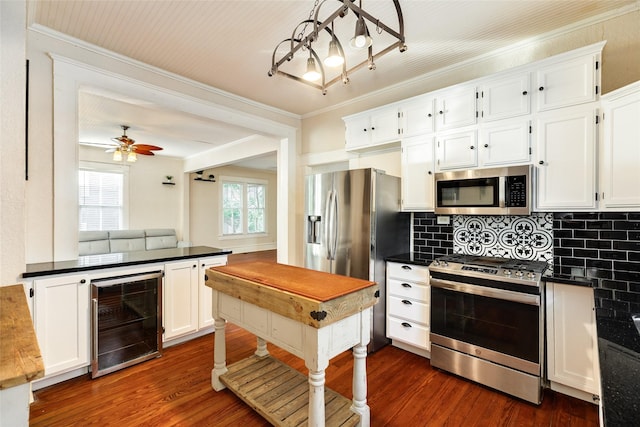 kitchen with appliances with stainless steel finishes, dark countertops, dark wood finished floors, white cabinets, and wine cooler
