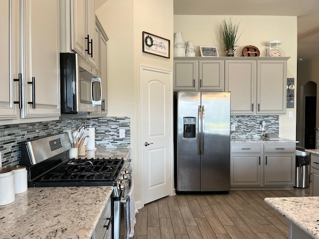 12813 Narrow Cove Dr, Texas City, TX 77568 - kitchen featuring appliances with stainless steel finishes, tasteful backsplash, light wood finished floors, light stone counters, and gray cabinets