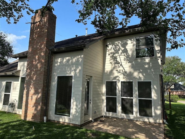 rear view of house with roof with shingles, a yard, and a chimney