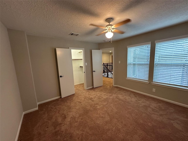 unfurnished bedroom with a walk in closet, a textured ceiling, carpet, baseboards, and visible vents