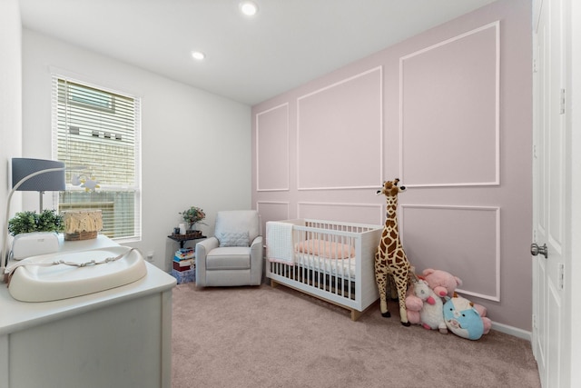 bedroom with a crib, light carpet, a decorative wall, and recessed lighting