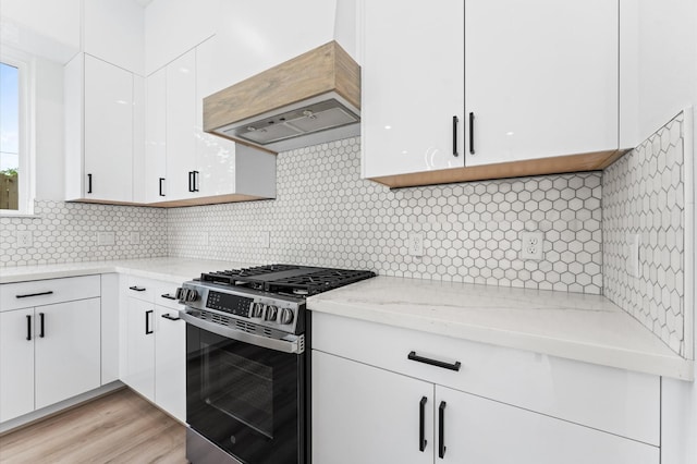 kitchen with custom exhaust hood, light stone countertops, stainless steel range with gas cooktop, white cabinets, and backsplash