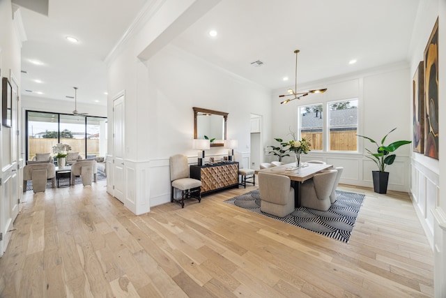 dining space with crown molding, light wood-style flooring, a decorative wall, and a chandelier