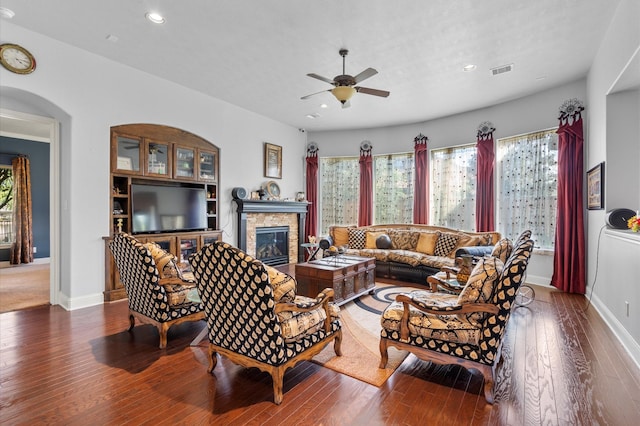 living room featuring ceiling fan, a stone fireplace, baseboards, visible vents, and hardwood / wood-style flooring