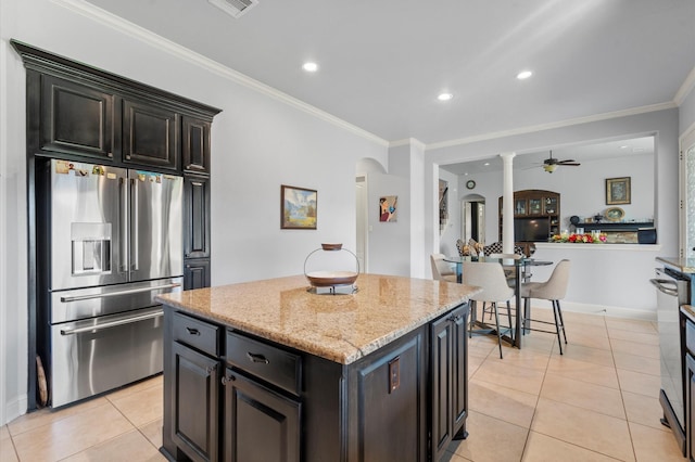 kitchen with ornamental molding, stainless steel refrigerator with ice dispenser, a center island, arched walkways, and light tile patterned floors