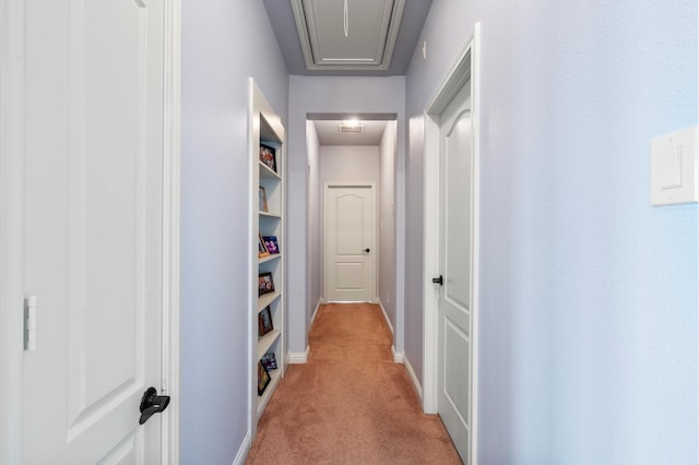 hallway with baseboards, attic access, and light colored carpet