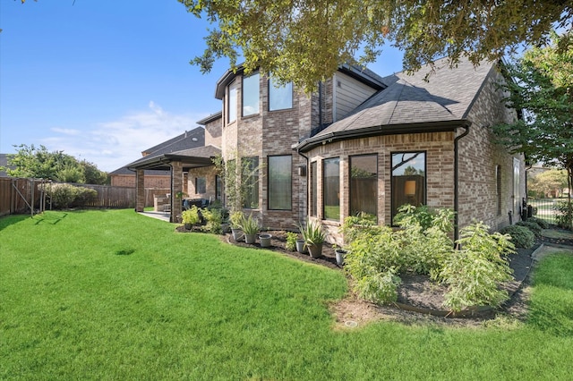 rear view of house with a lawn, a fenced backyard, brick siding, and a shingled roof