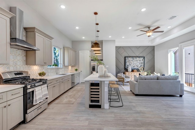 kitchen with ceiling fan, appliances with stainless steel finishes, beverage cooler, wall chimney exhaust hood, and open floor plan