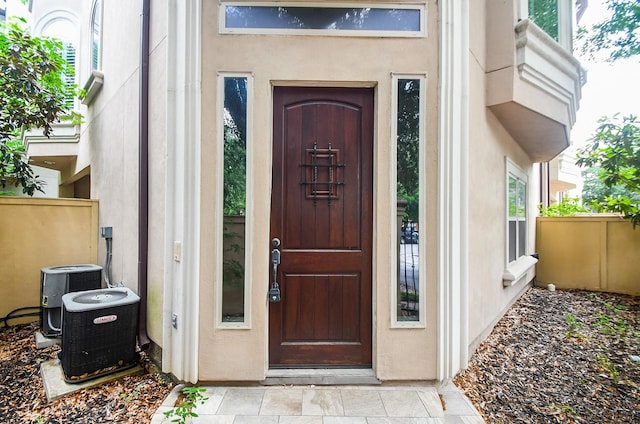 entrance to property with fence, cooling unit, and stucco siding