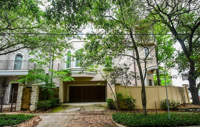view of front of home with fence, a garage, stucco siding, concrete driveway, and a balcony